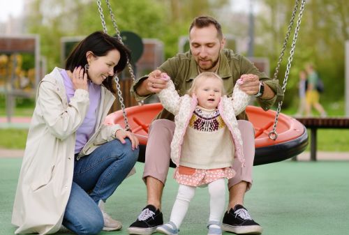 Toddler girl having fun on outdoor playground with parents - Adult step parent adoption concept
