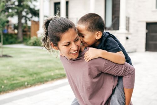 mom giving son a piggy back ride - adoption, guardianship, and custody concept