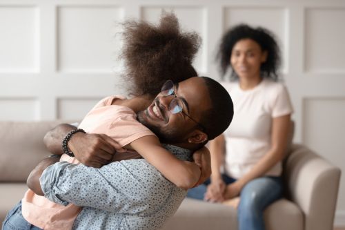 Happy dad embracing daughter with mother smiling in background - child custody conflict concept