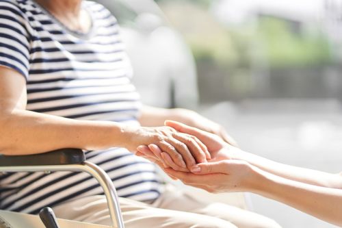 Hands of caregiver and elderly person in wheelchair holding hands. Adult guardianship concept.