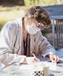 Elderly woman wears a surgical mask as protection during the COVID-19 while filling out documents